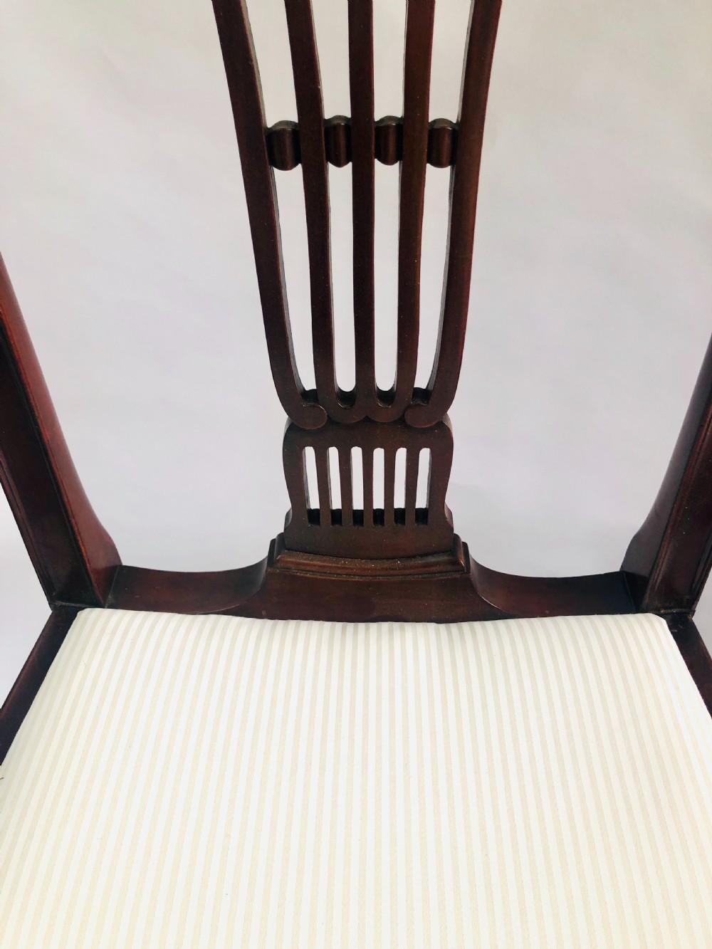 A set of four dark mahogany dining chairs featuring carved fan splats, cream upholstered seats, and tapered legs. View VIII