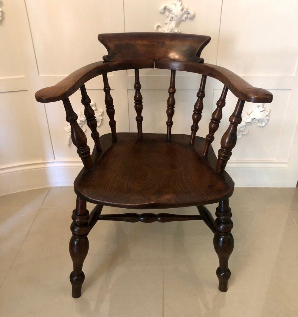 An antique dark oak captains desk chair featuring a curved crest rail, turned spindles, a contoured saddle seat, and sturdy turned legs.