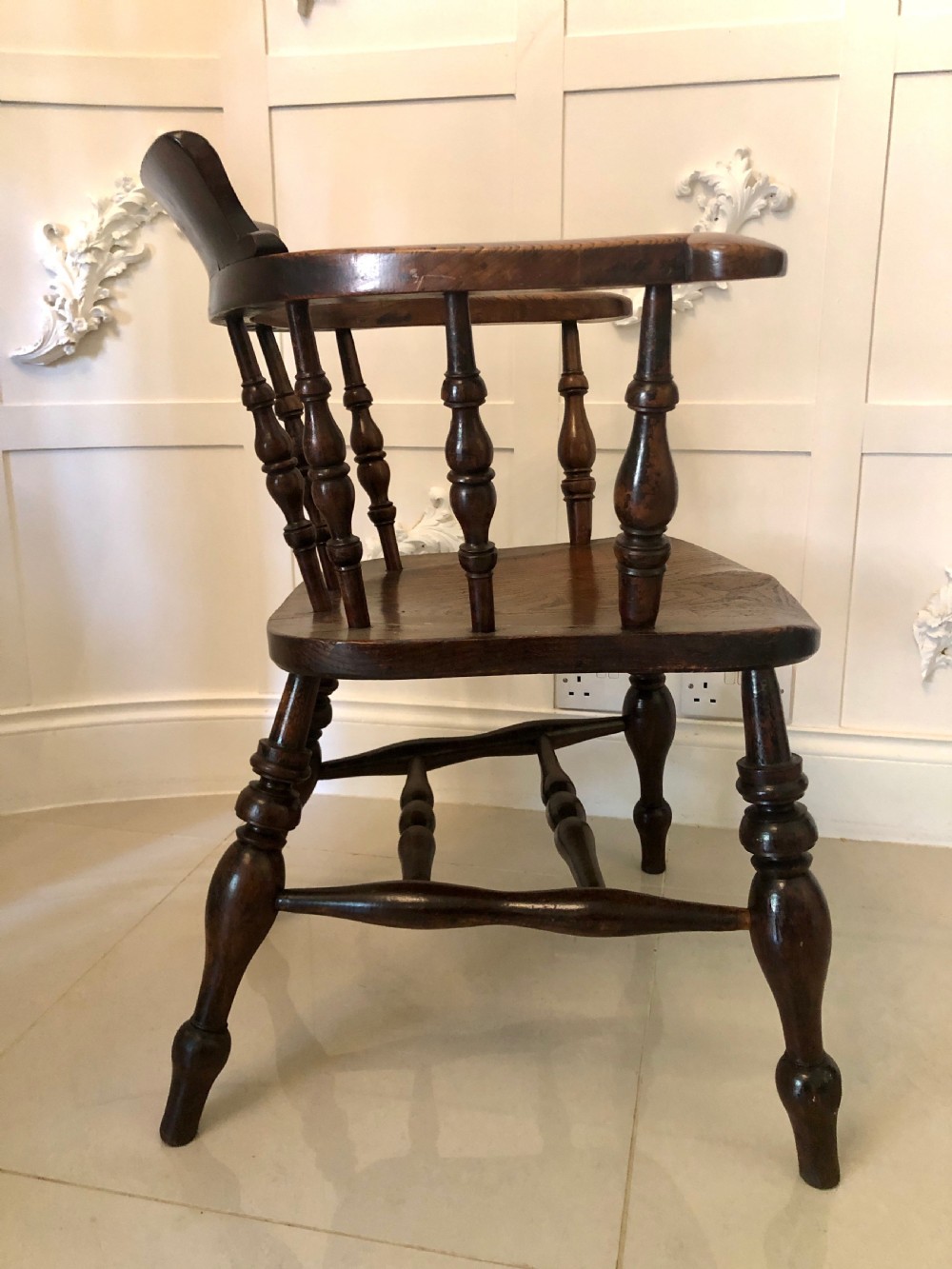 An antique dark oak captains desk chair featuring a curved crest rail, turned spindles, a contoured saddle seat, and sturdy turned legs. View VII