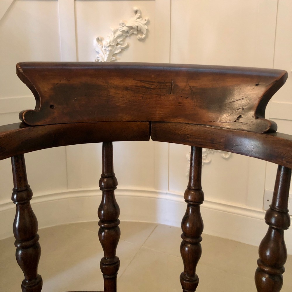 An antique dark oak captains desk chair featuring a curved crest rail, turned spindles, a contoured saddle seat, and sturdy turned legs. View X