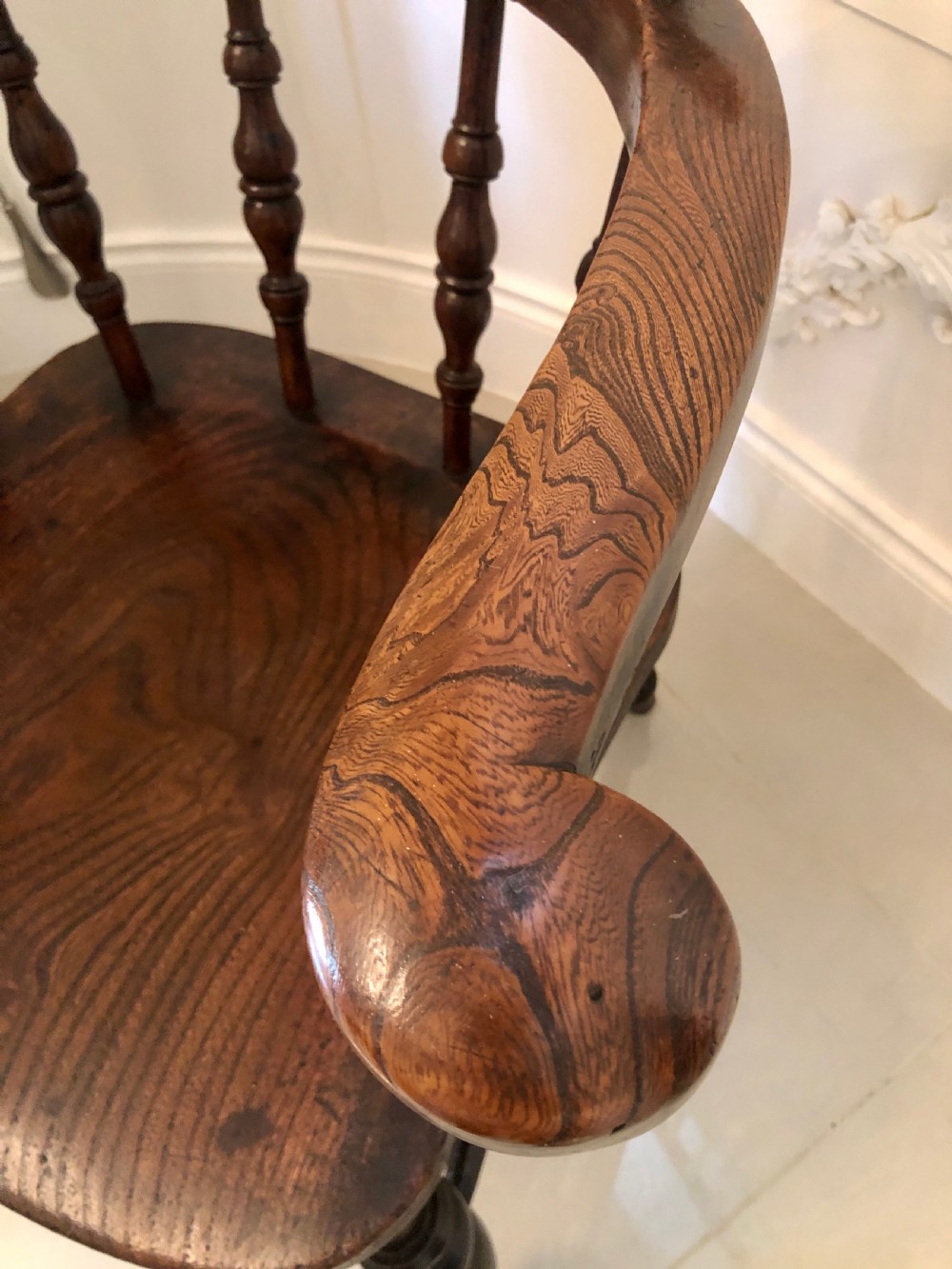 An antique dark oak captains desk chair featuring a curved crest rail, turned spindles, a contoured saddle seat, and sturdy turned legs. View XI