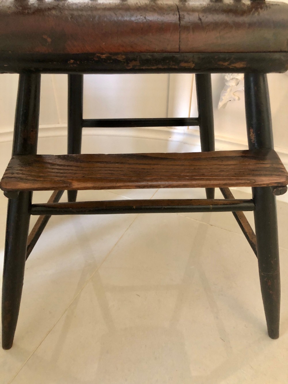 A dark-stained wooden antique child high chair featuring a vertical spindle backrest, armrests, splayed legs, and a built-in wooden footrest. View II