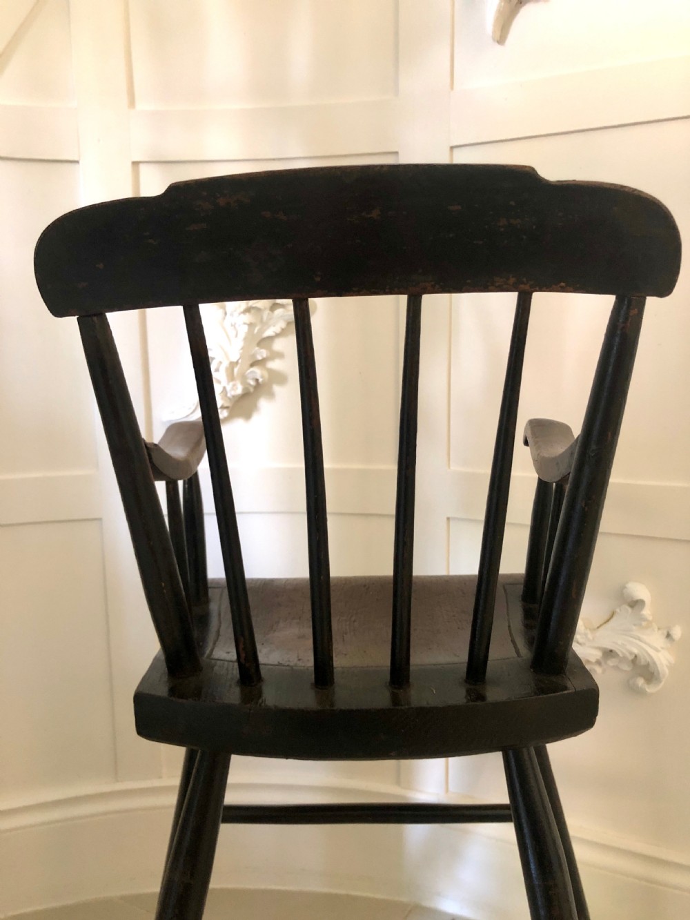 A dark-stained wooden antique child high chair featuring a vertical spindle backrest, armrests, splayed legs, and a built-in wooden footrest. View V