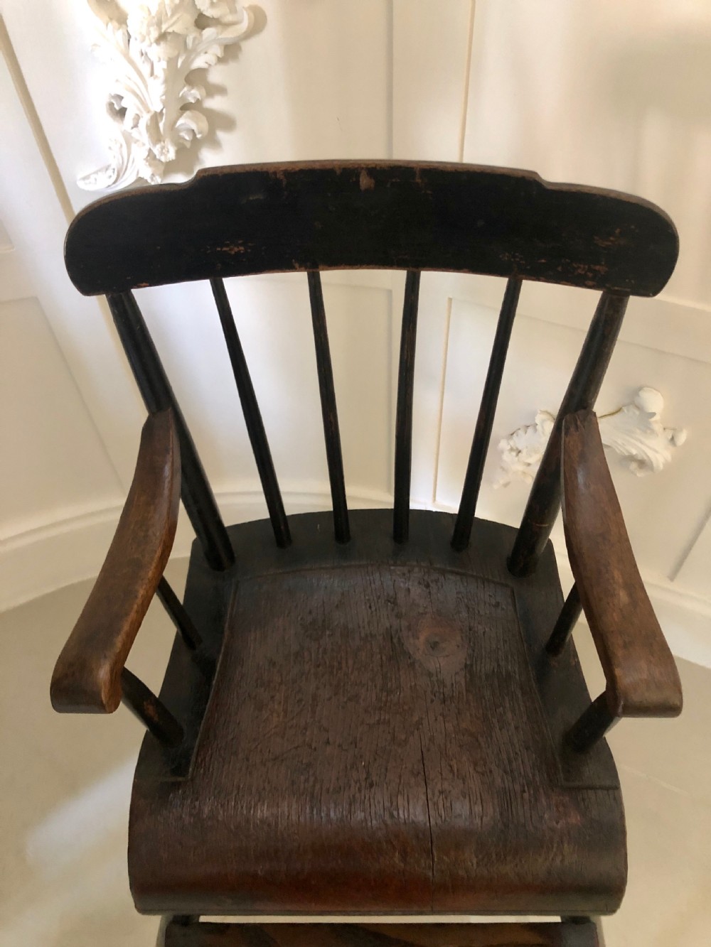 A dark-stained wooden antique child high chair featuring a vertical spindle backrest, armrests, splayed legs, and a built-in wooden footrest. View VI