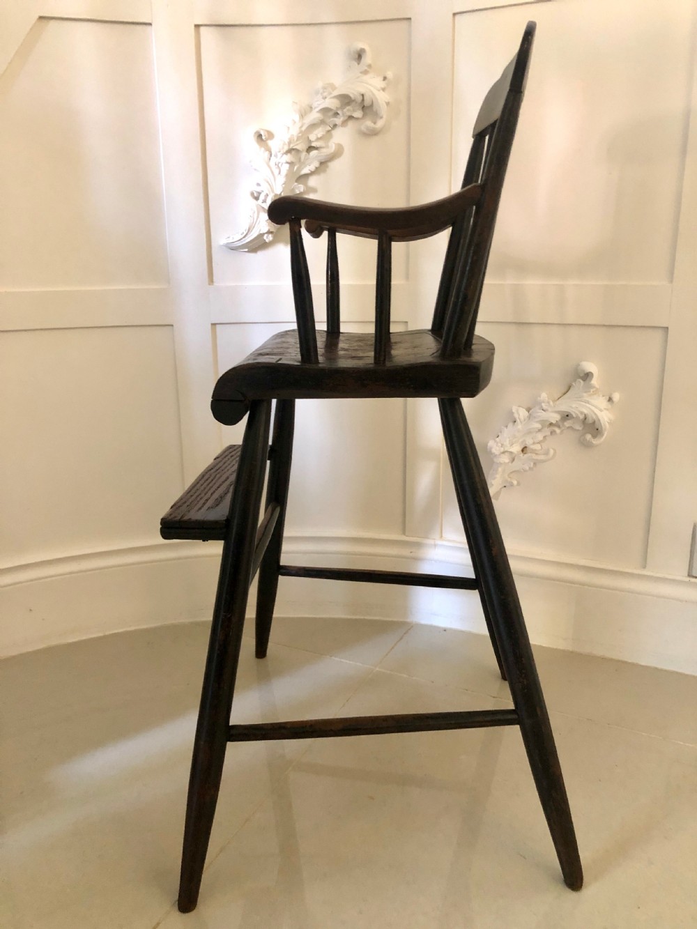 A dark-stained wooden antique child high chair featuring a vertical spindle backrest, armrests, splayed legs, and a built-in wooden footrest. View VIII