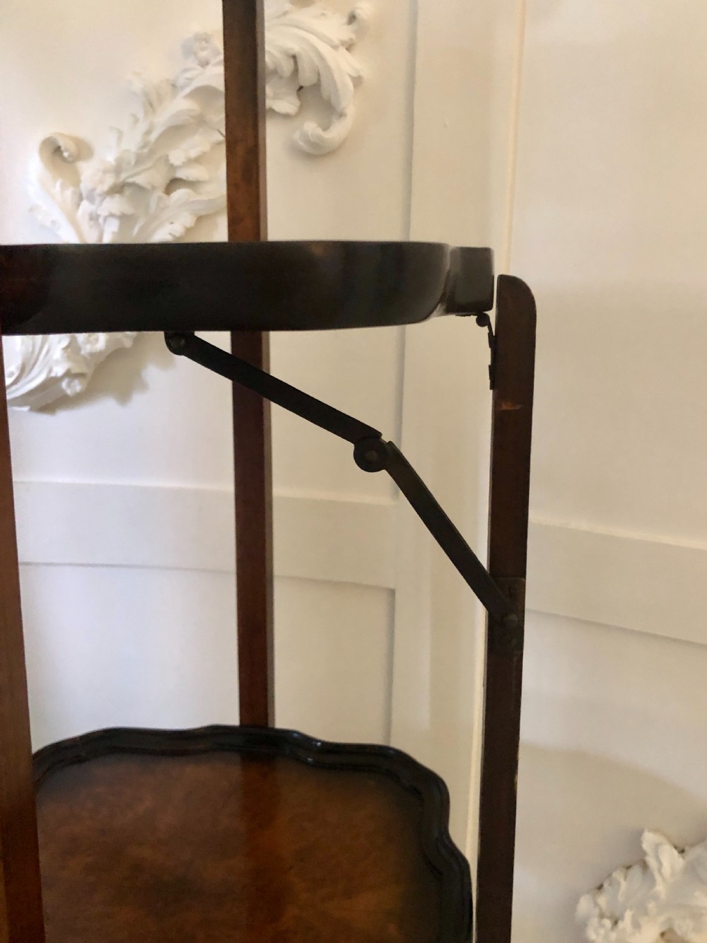 An antique three-tier walnut folding cake stand featuring shaped moulded trays, a curved top carrying handle, and straight wooden side supports. View X