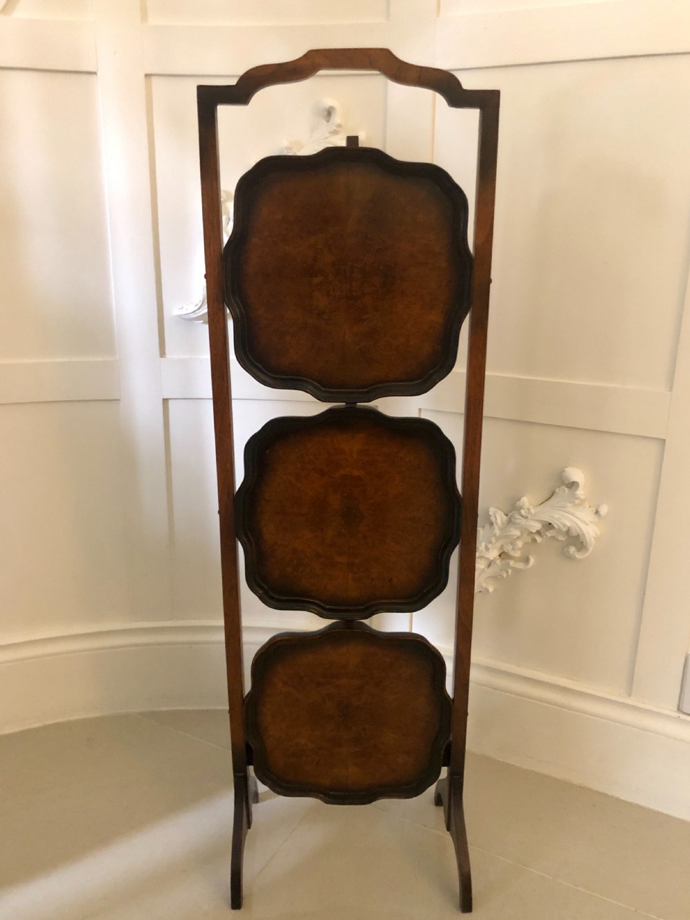 An antique three-tier walnut folding cake stand featuring shaped moulded trays, a curved top carrying handle, and straight wooden side supports. View XIII