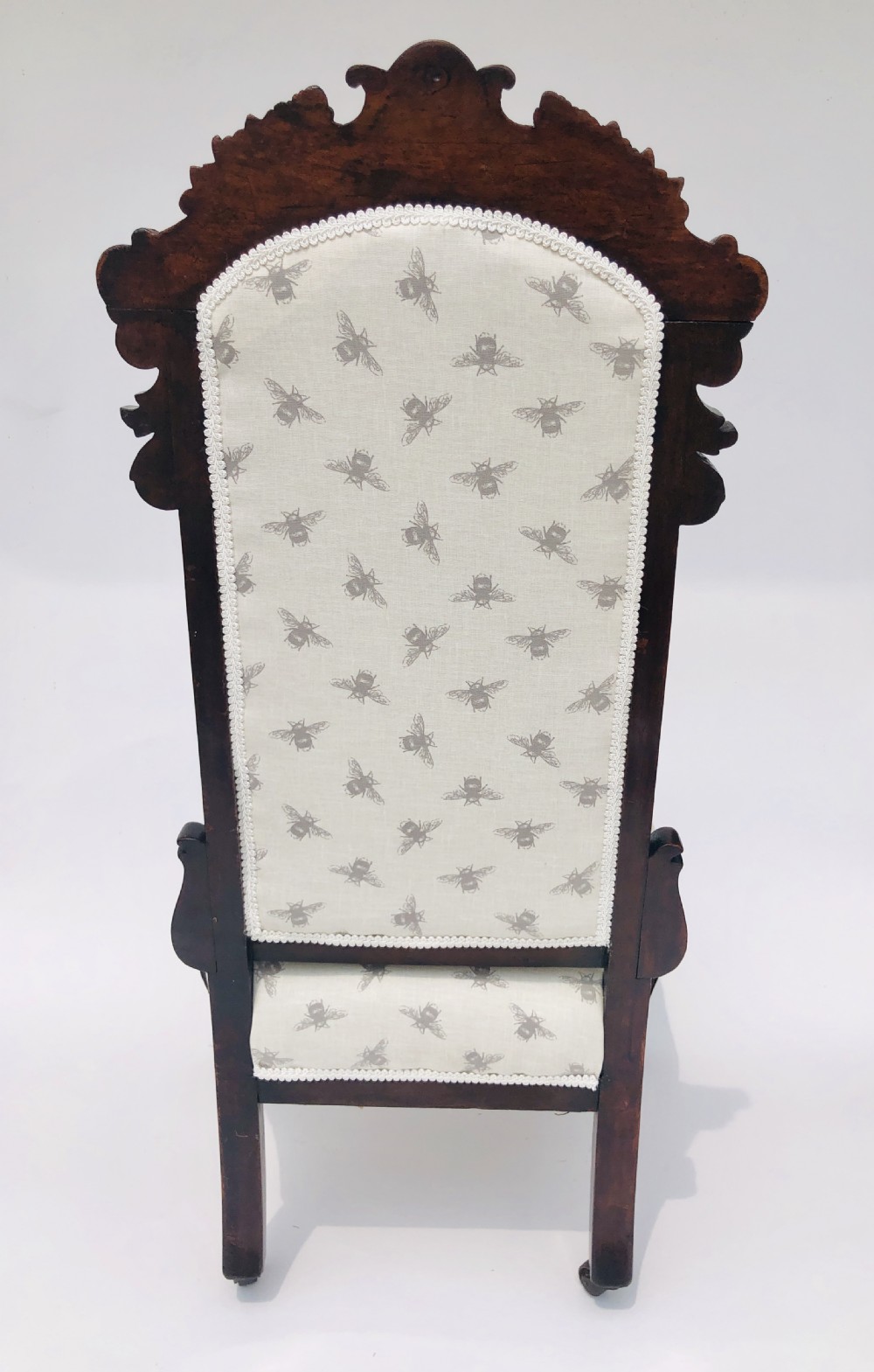 A Victorian carved rosewood ladies chair featuring a high upholstered backrest and seat with a grey bee pattern on cream fabric, raised on cabriole front legs with brass castors. View V