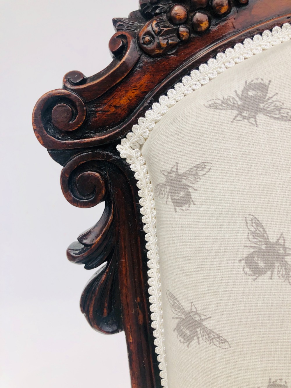 A Victorian carved rosewood ladies chair featuring a high upholstered backrest and seat with a grey bee pattern on cream fabric, raised on cabriole front legs with brass castors. View VI