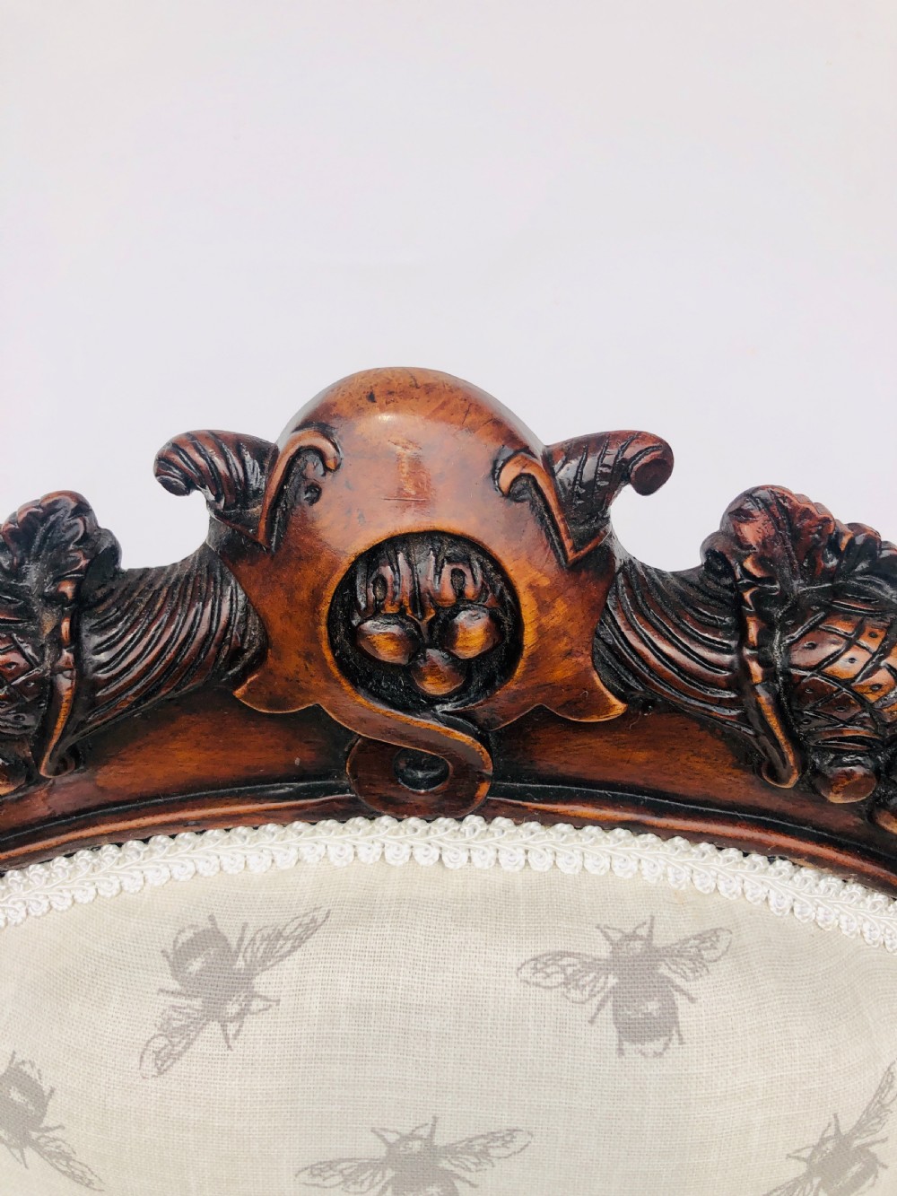 A Victorian carved rosewood ladies chair featuring a high upholstered backrest and seat with a grey bee pattern on cream fabric, raised on cabriole front legs with brass castors. View VII