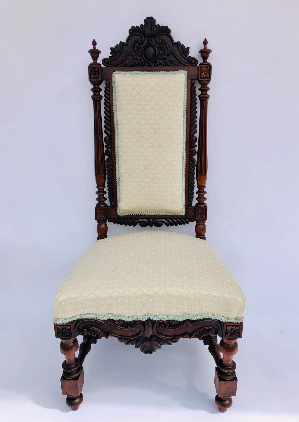 A Victorian carved rosewood side chair featuring a high back with ornate carved cresting, turned side columns, and light cream pattern upholstered seating.