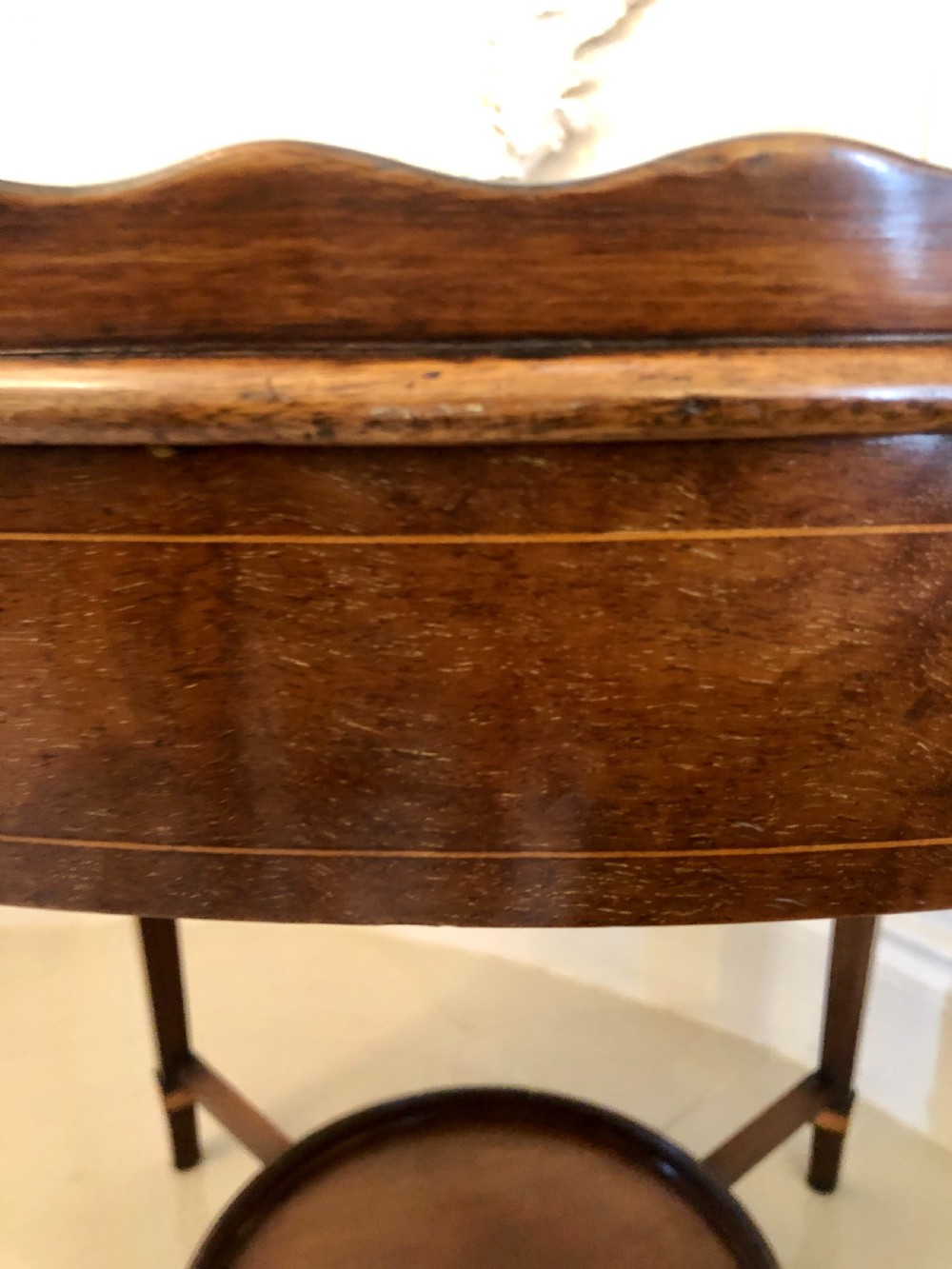 An Edwardian oval mahogany tray table with brass carrying handles, satinwood inlay, tapered legs, and a lower circular tier. View VI
