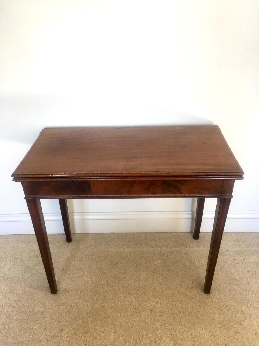 An 18th-century George III mahogany side table featuring a fold-over rectangular top, veneered apron, and four tapered square legs.