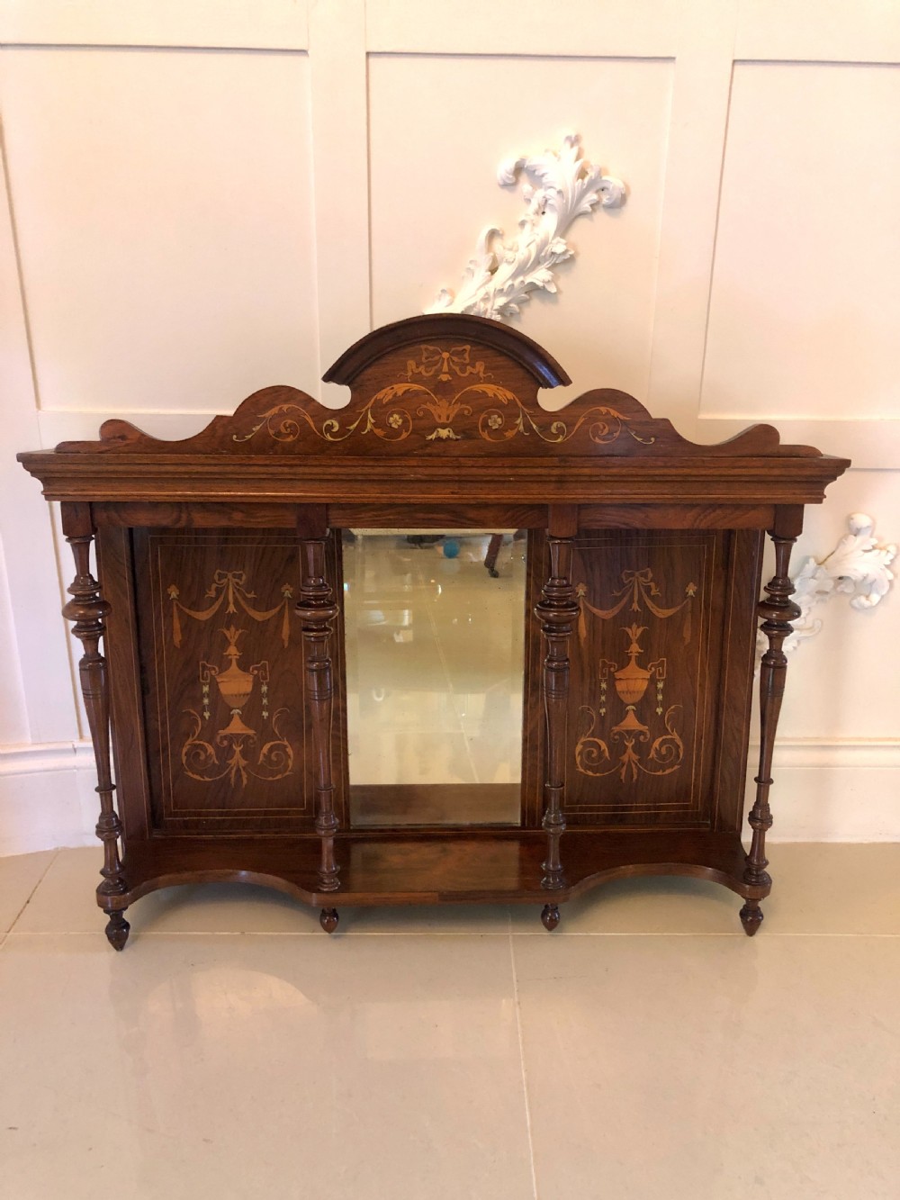 An Edwardian rosewood overmantel mirror featuring detailed bow and urn marquetry inlays, turned supporting columns, and a central rectangular glass plate.