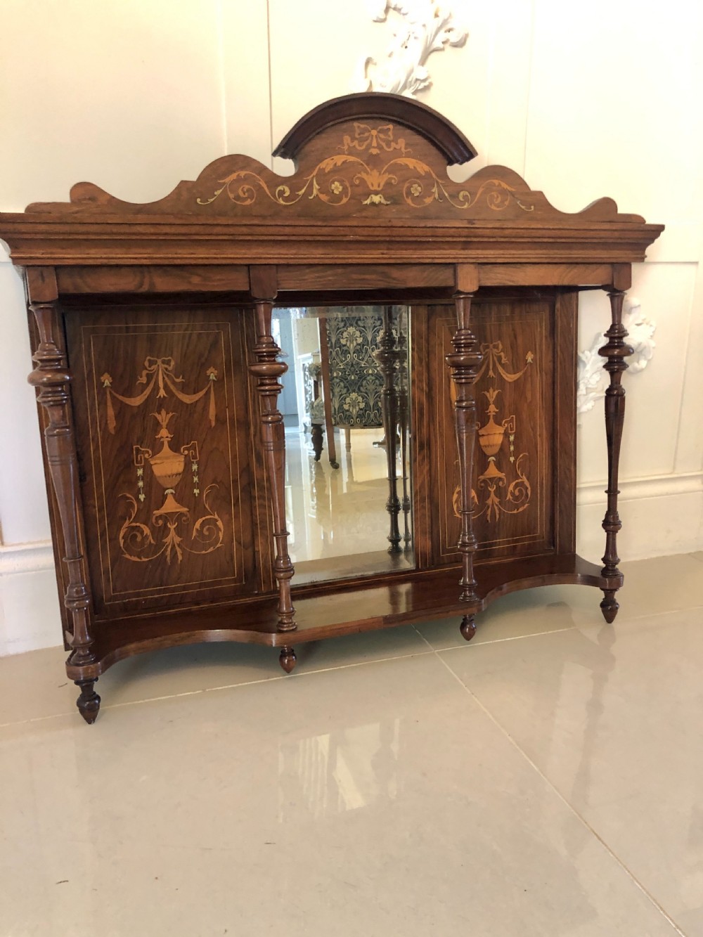 An Edwardian rosewood overmantel mirror featuring detailed bow and urn marquetry inlays, turned supporting columns, and a central rectangular glass plate. View II