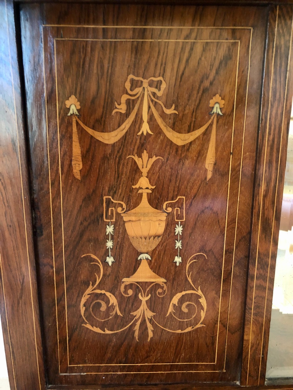 An Edwardian rosewood overmantel mirror featuring detailed bow and urn marquetry inlays, turned supporting columns, and a central rectangular glass plate. View VII