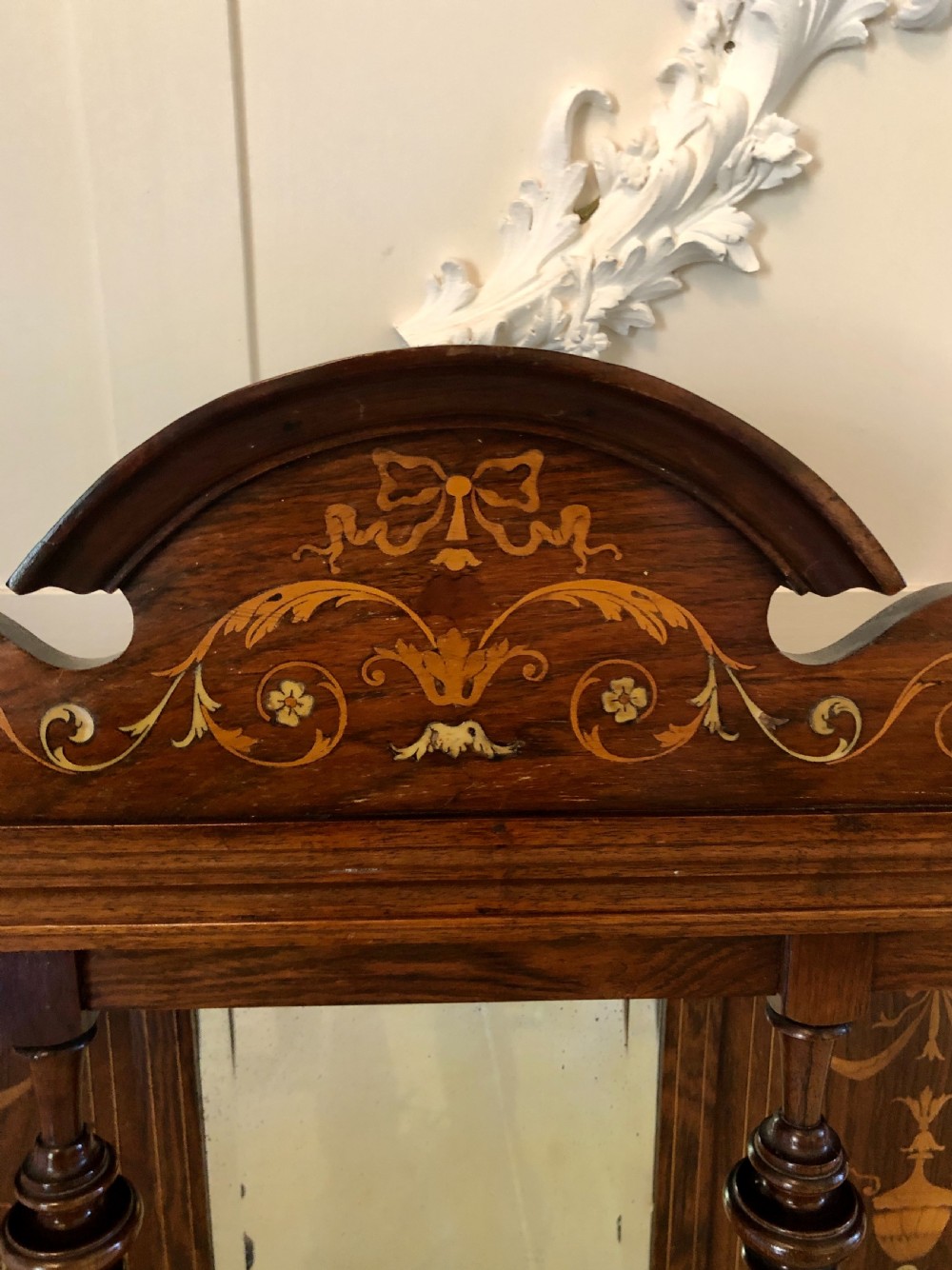 An Edwardian rosewood overmantel mirror featuring detailed bow and urn marquetry inlays, turned supporting columns, and a central rectangular glass plate. View IX