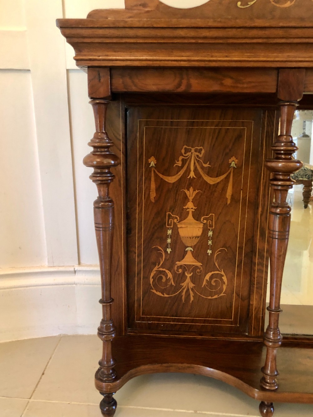 An Edwardian rosewood overmantel mirror featuring detailed bow and urn marquetry inlays, turned supporting columns, and a central rectangular glass plate. View X