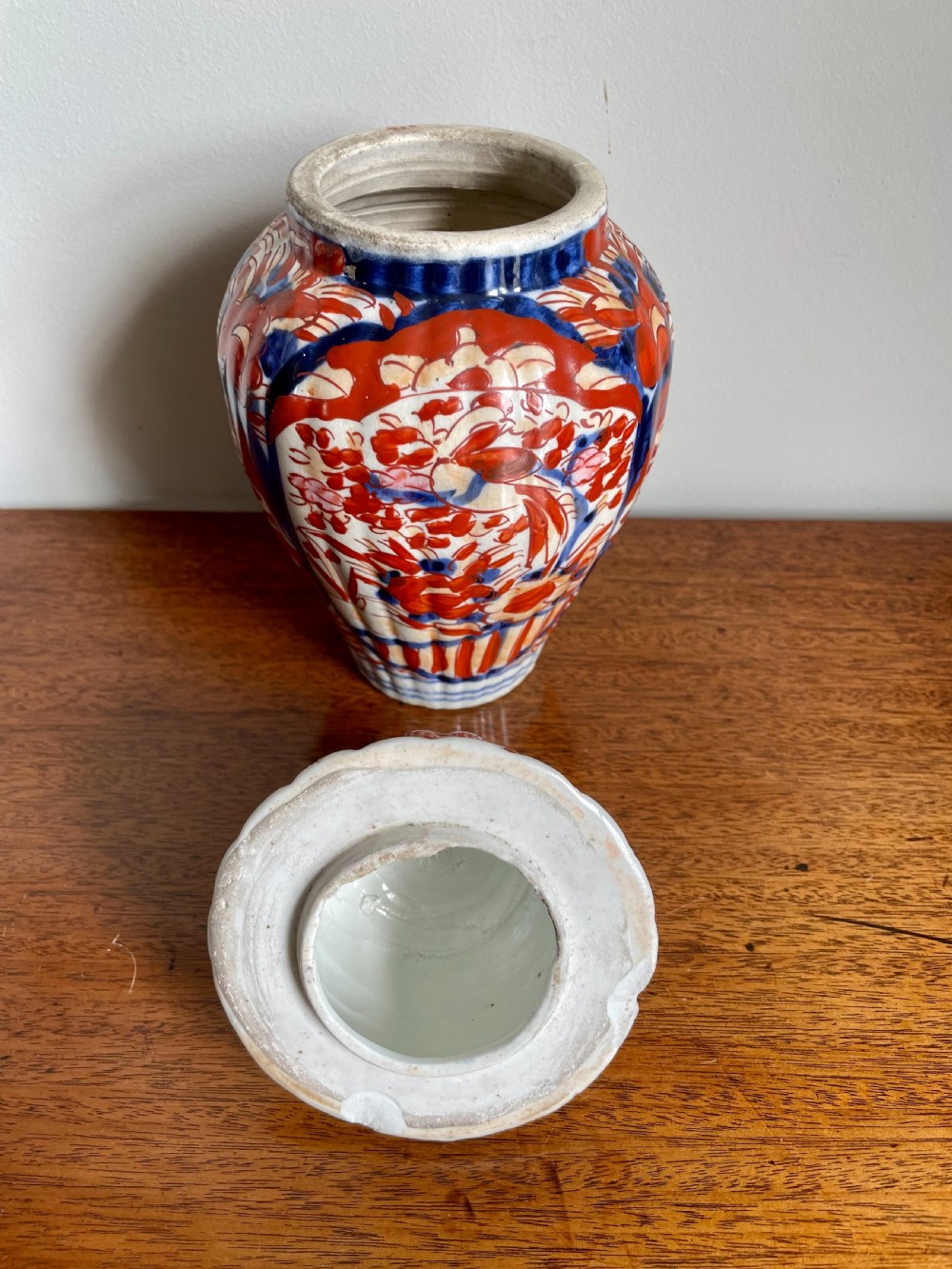 A fluted ceramic Imari vase with a matching lid, decorated in hand-painted floral patterns of iron-red and cobalt blue on a white background. View II