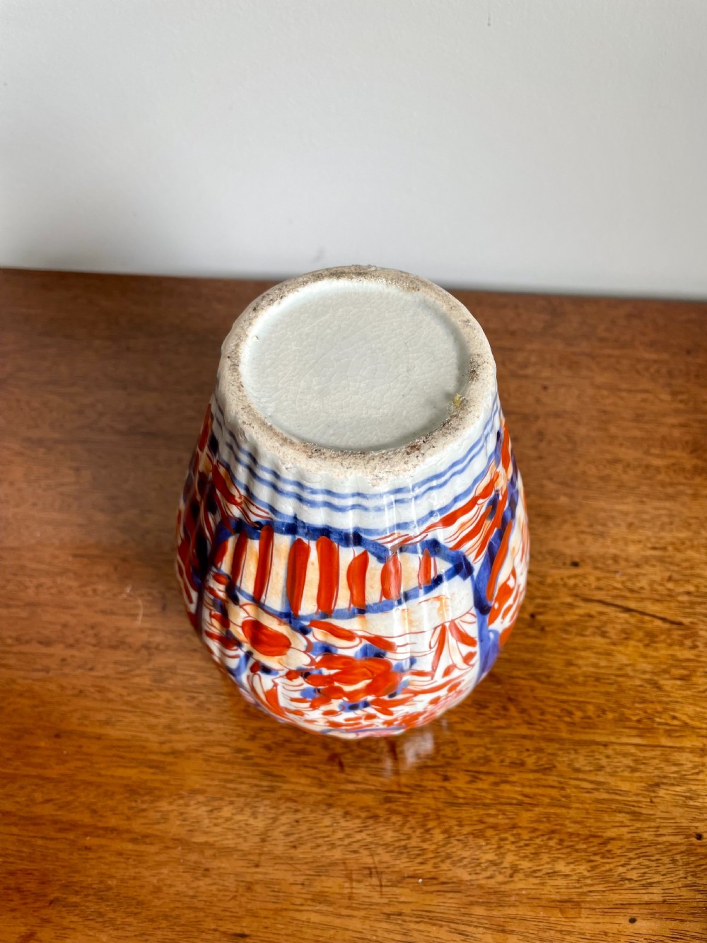 A fluted ceramic Imari vase with a matching lid, decorated in hand-painted floral patterns of iron-red and cobalt blue on a white background. View V