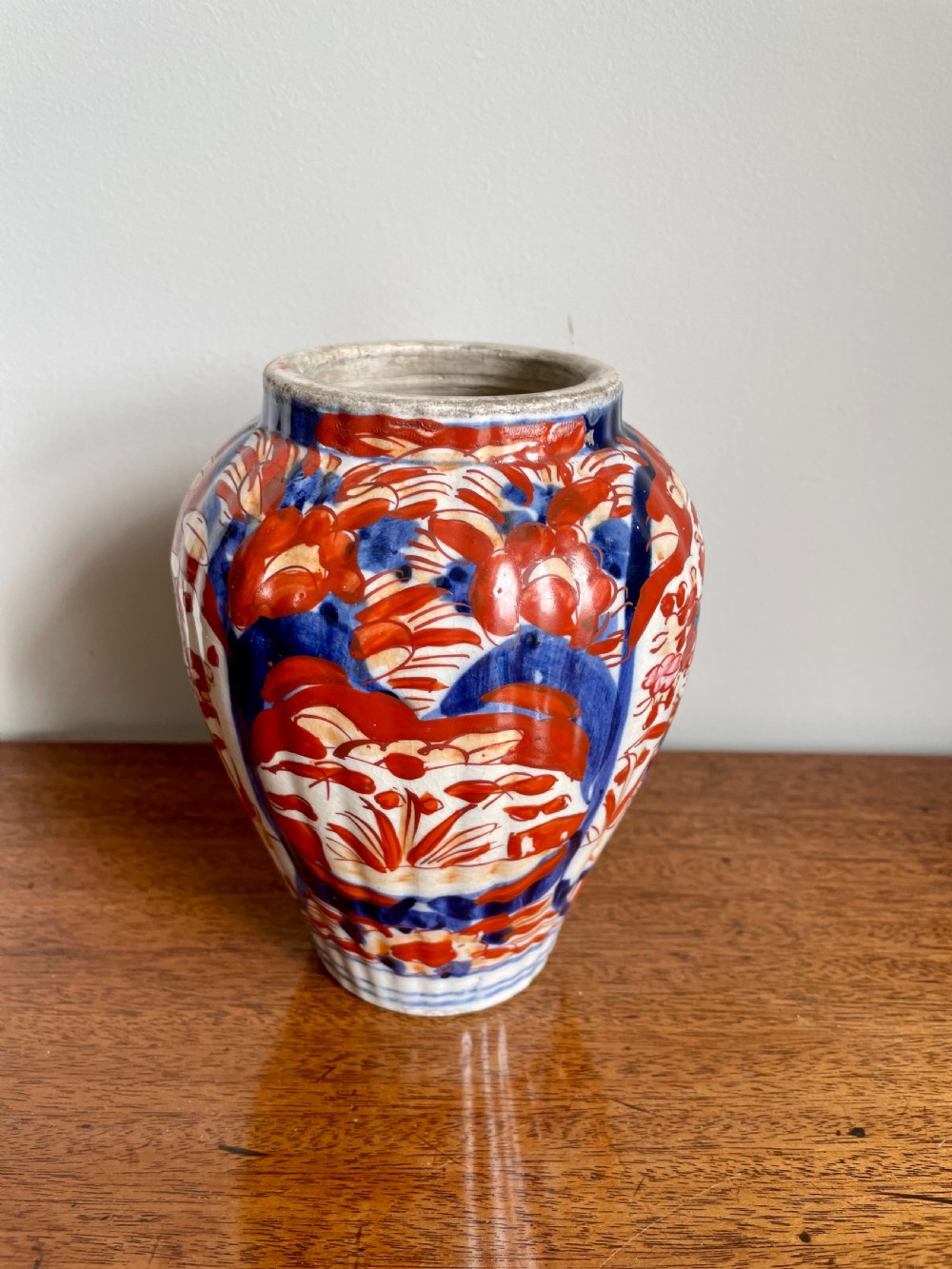 A fluted ceramic Imari vase with a matching lid, decorated in hand-painted floral patterns of iron-red and cobalt blue on a white background. View VI