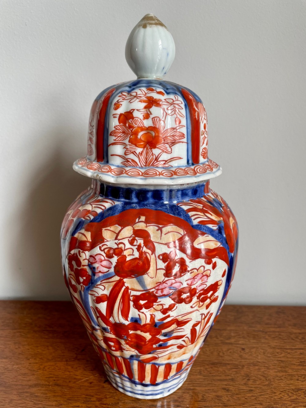 A fluted ceramic Imari vase with a matching lid, decorated in hand-painted floral patterns of iron-red and cobalt blue on a white background. View VIII