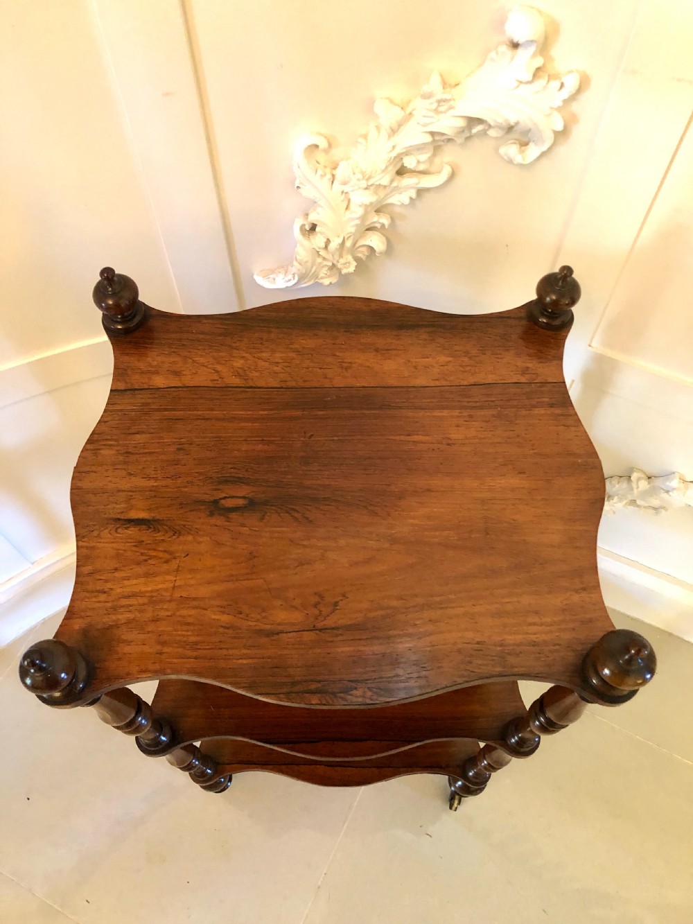 A three-tiered Victorian rosewood whatnot featuring serpentine shelf edges, turned corner supports, decorative finials, and brass castors. View III