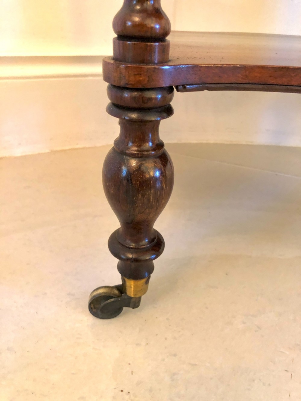 A three-tiered Victorian rosewood whatnot featuring serpentine shelf edges, turned corner supports, decorative finials, and brass castors. View VI