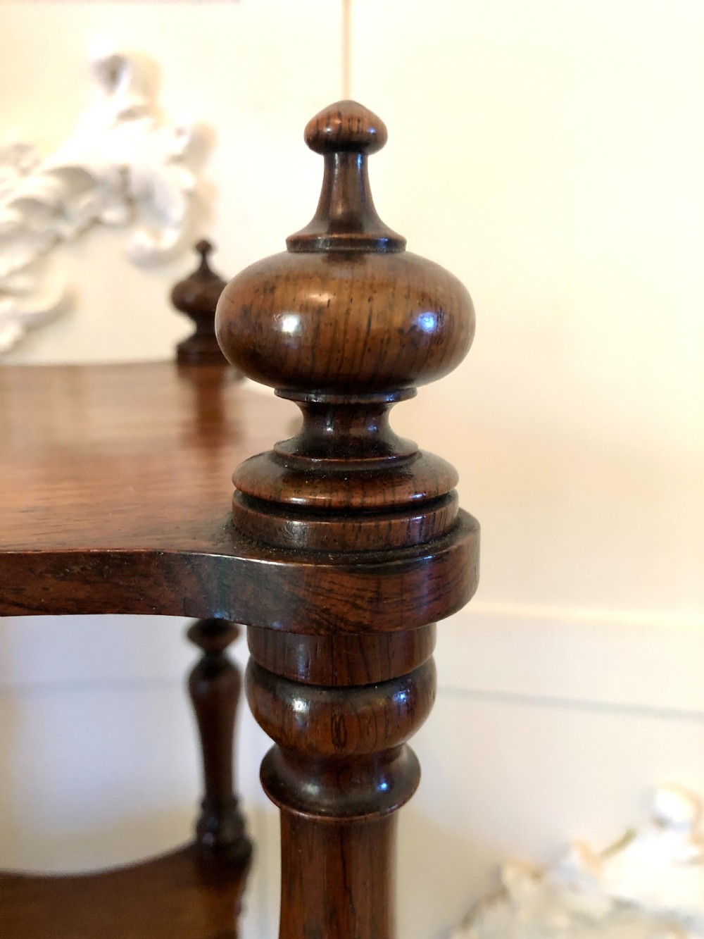 A three-tiered Victorian rosewood whatnot featuring serpentine shelf edges, turned corner supports, decorative finials, and brass castors. View VII