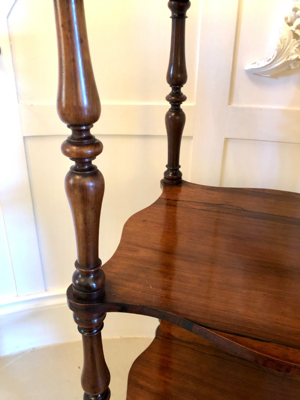 A three-tiered Victorian rosewood whatnot featuring serpentine shelf edges, turned corner supports, decorative finials, and brass castors. View VIII