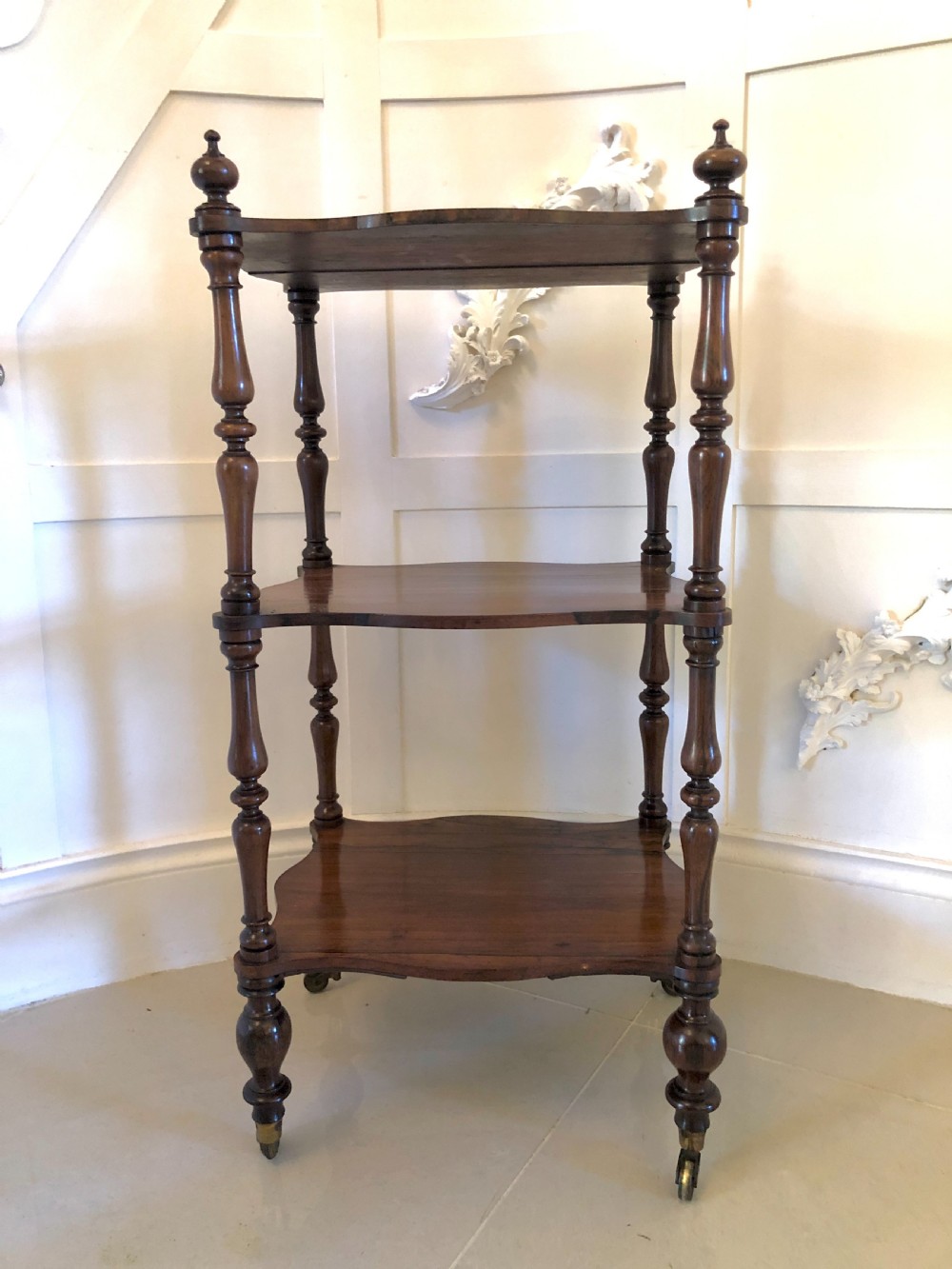 A three-tiered Victorian rosewood whatnot featuring serpentine shelf edges, turned corner supports, decorative finials, and brass castors. View XI