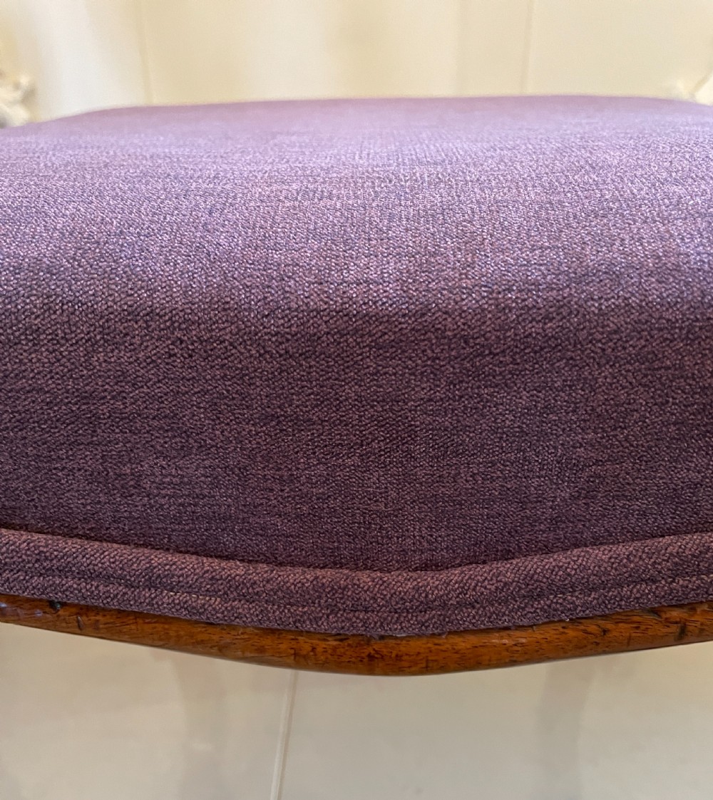 A square Victorian footstool with purple upholstery resting on carved walnut cabriole legs with scroll feet. View X