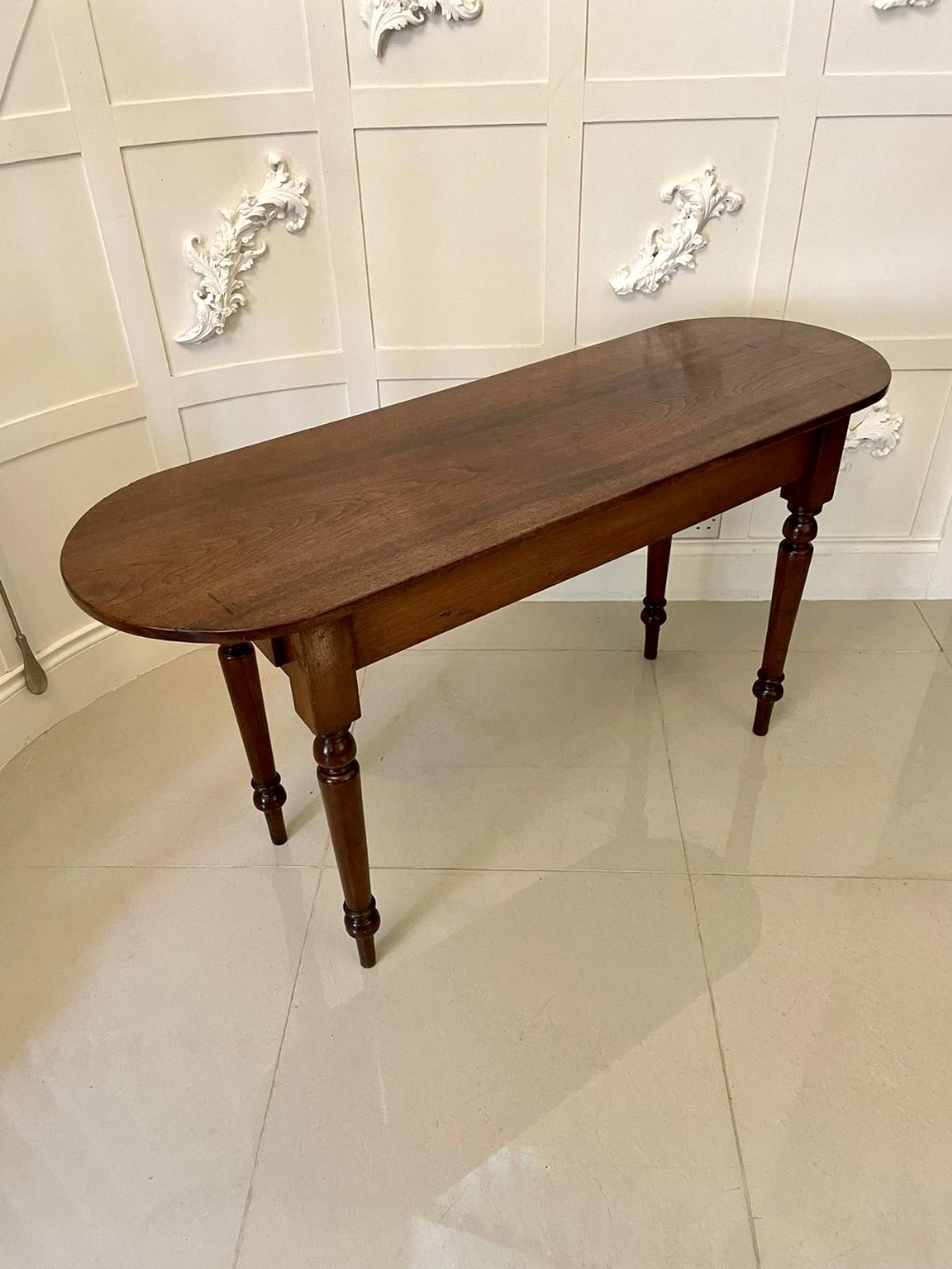 A long, narrow dark brown oak side table featuring a rounded top and four slender turned legs.