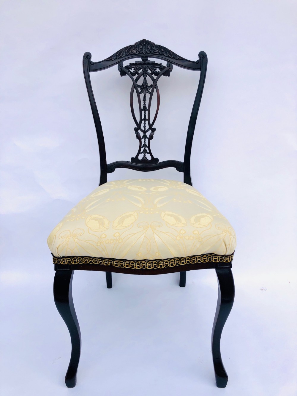 A pair of Victorian ebonised wood side chairs featuring intricate pierced back splats, carved crest rails, cream fabric seats, and cabriole front legs. View III