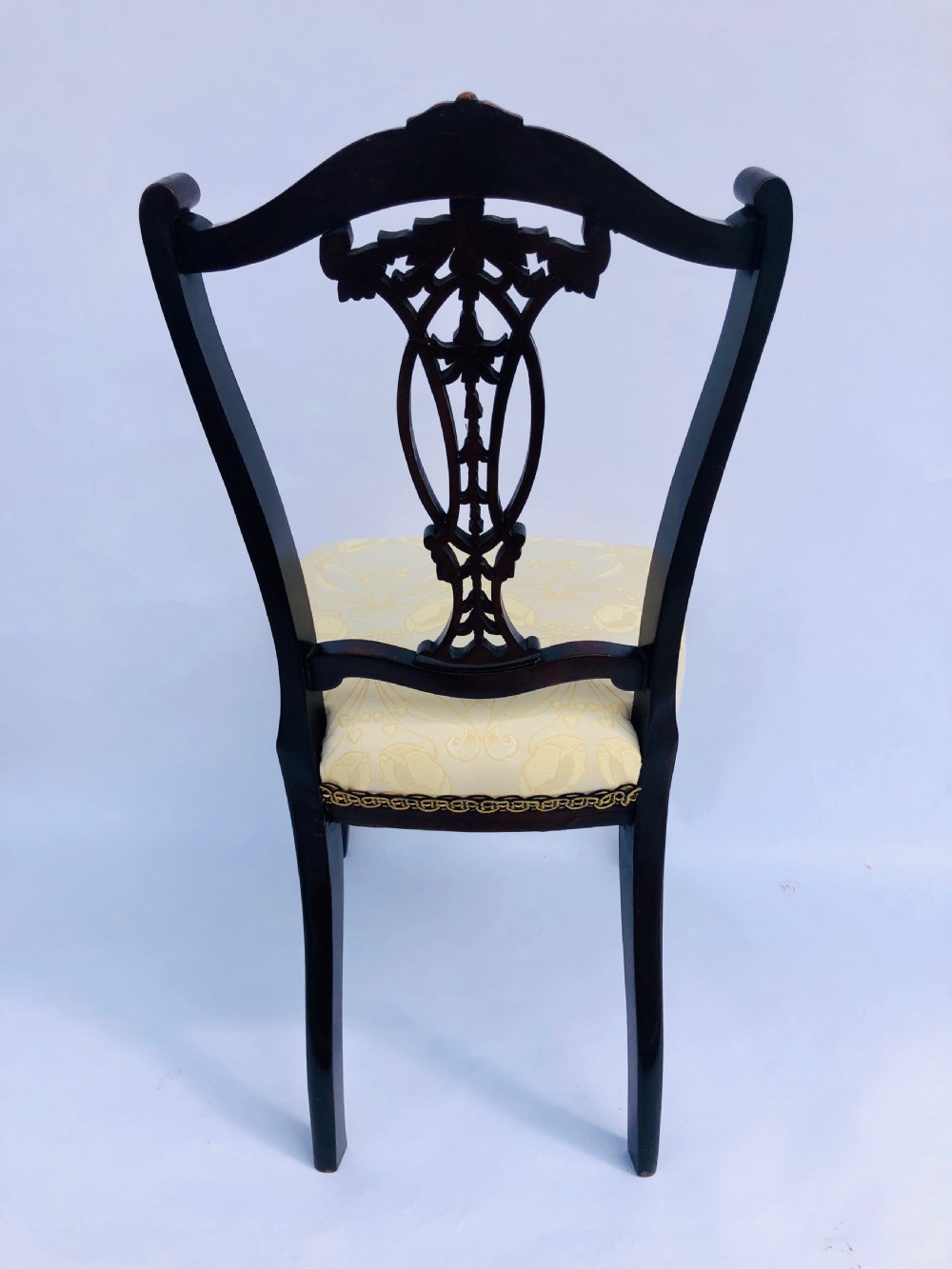 A pair of Victorian ebonised wood side chairs featuring intricate pierced back splats, carved crest rails, cream fabric seats, and cabriole front legs. View V