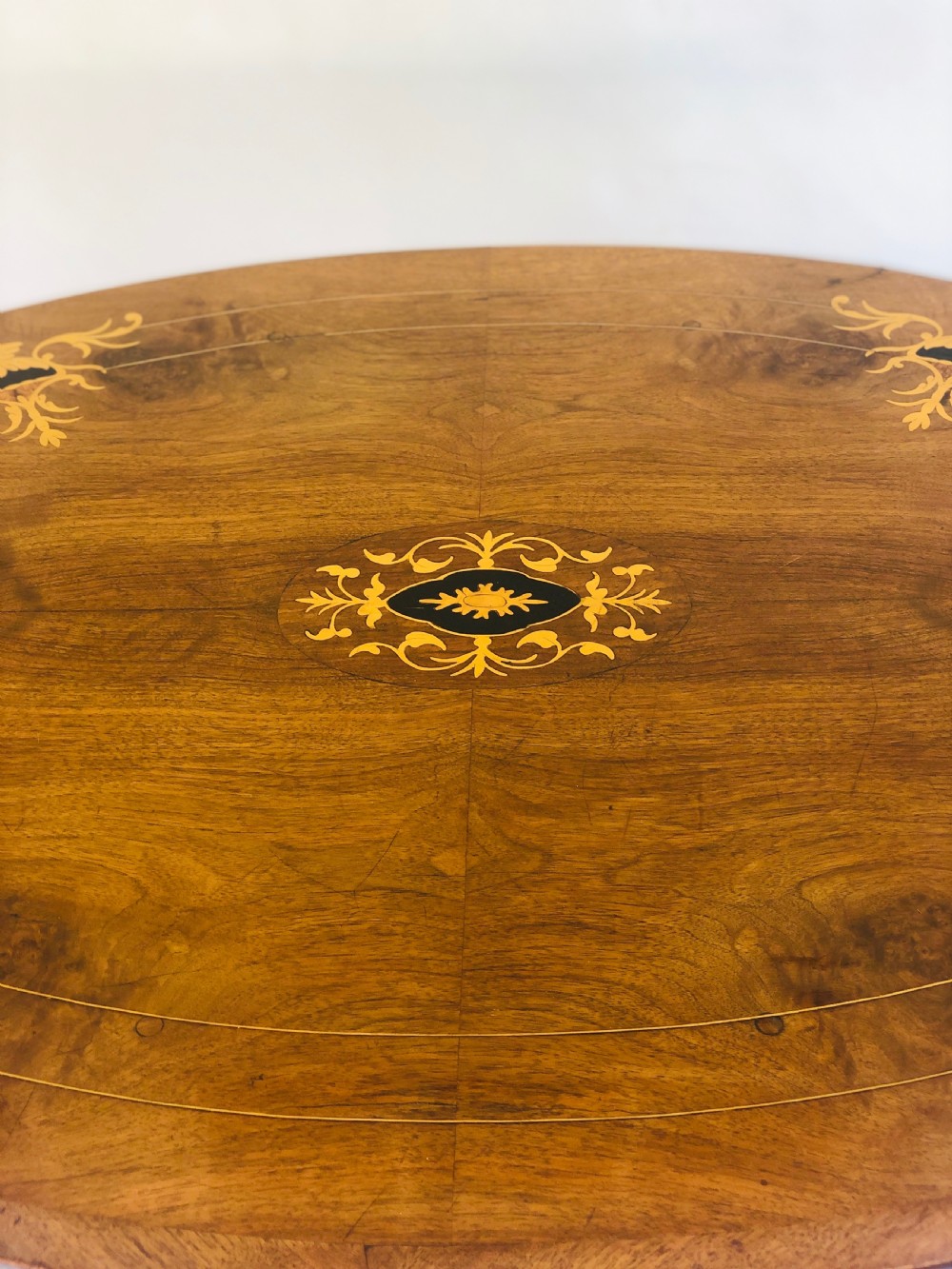 An oval Victorian walnut centre table featuring floral marquetry inlays on the top, supported by turned central columns and four carved legs on castors. View III