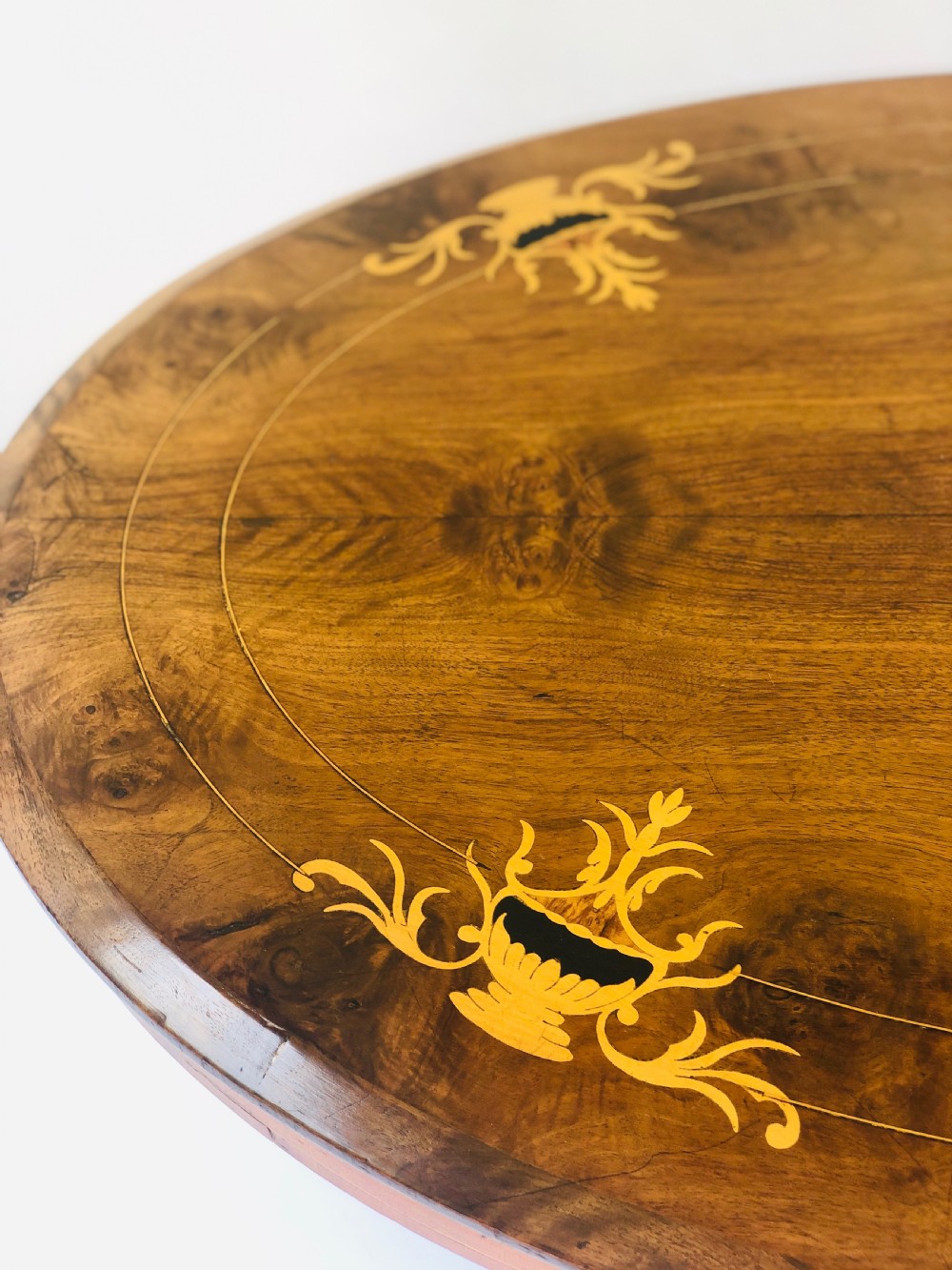An oval Victorian walnut centre table featuring floral marquetry inlays on the top, supported by turned central columns and four carved legs on castors. View V