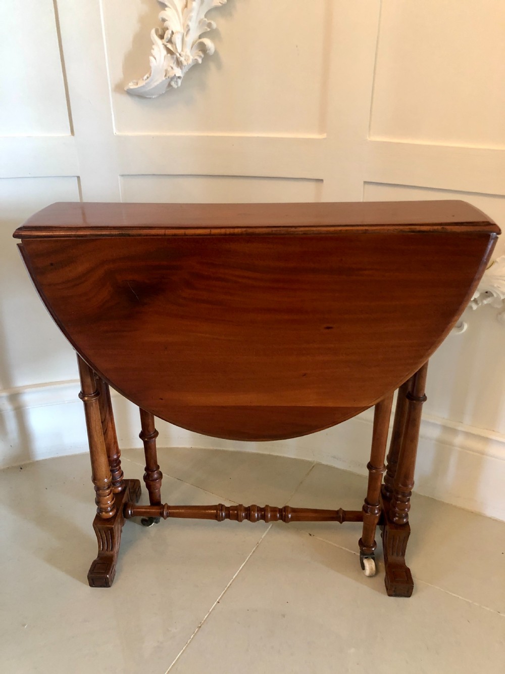 A Victorian walnut Sutherland table with drop leaves folded down, set on turned legs and ceramic castors. View II