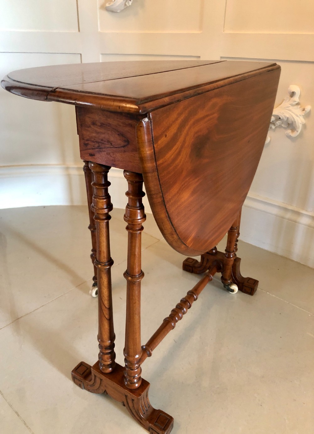 A Victorian walnut Sutherland table with drop leaves folded down, set on turned legs and ceramic castors. View V