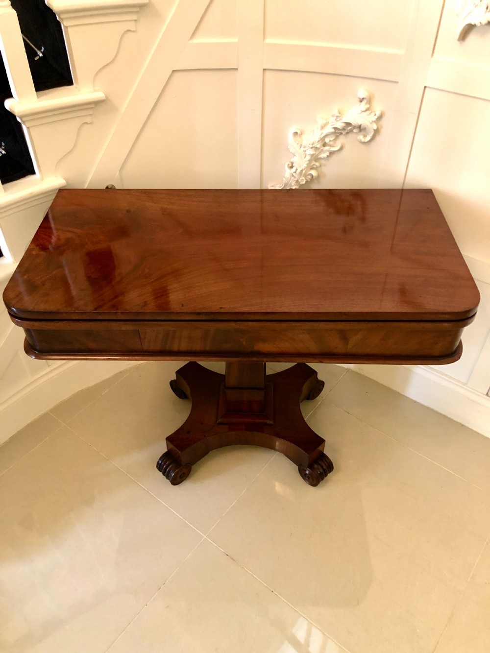 A William IV mahogany fold-over tea table featuring a rectangular swivel top on a square pedestal and a quadruped base with scrolled feet.