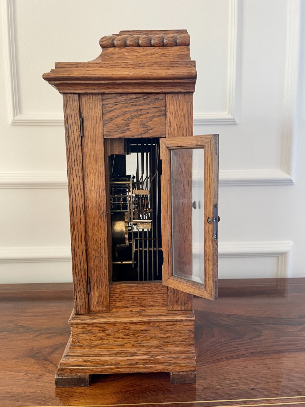 A Victorian carved oak bracket clock featuring a silvered engraved dial with Roman numerals, a chime-silent secondary dial, and carved gadrooned detailing along the top base. View III