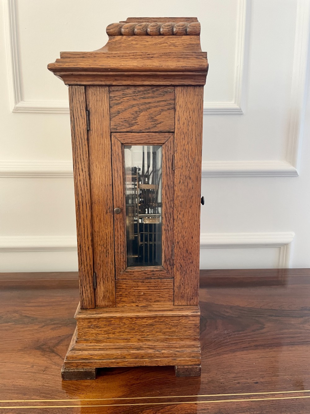 A Victorian carved oak bracket clock featuring a silvered engraved dial with Roman numerals, a chime-silent secondary dial, and carved gadrooned detailing along the top base. View VII