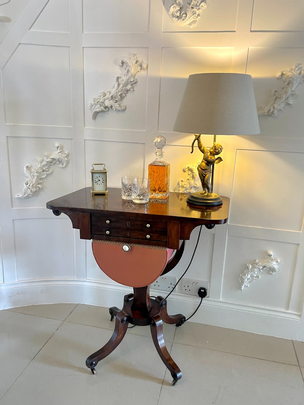 An antique Regency rosewood sewing table featuring small drop leaves, drawers with brass handles, a terracotta fabric work basket below, and a pedestal base with four splayed legs on castors. View II