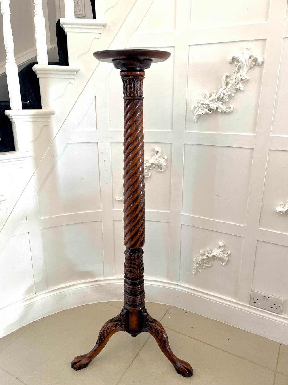A tall Victorian mahogany torchere stand featuring a circular top, spiral twist central column, carved leaf details, and a tripod base.