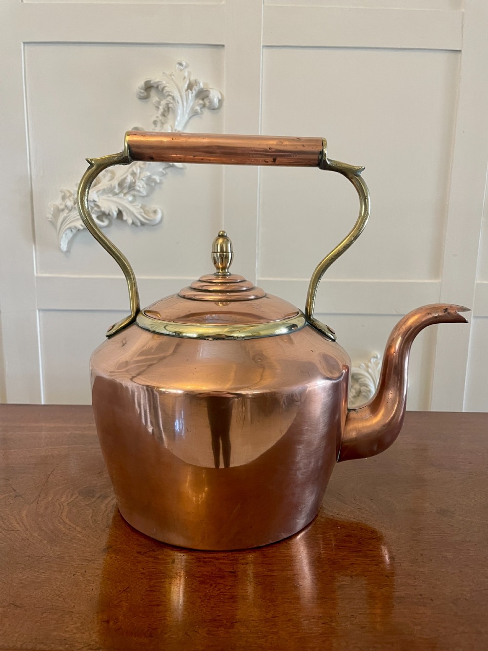 A George III copper tea kettle featuring a brass-accented overhead handle, a gooseneck spout, and a stepped lid with a brass finial. View X