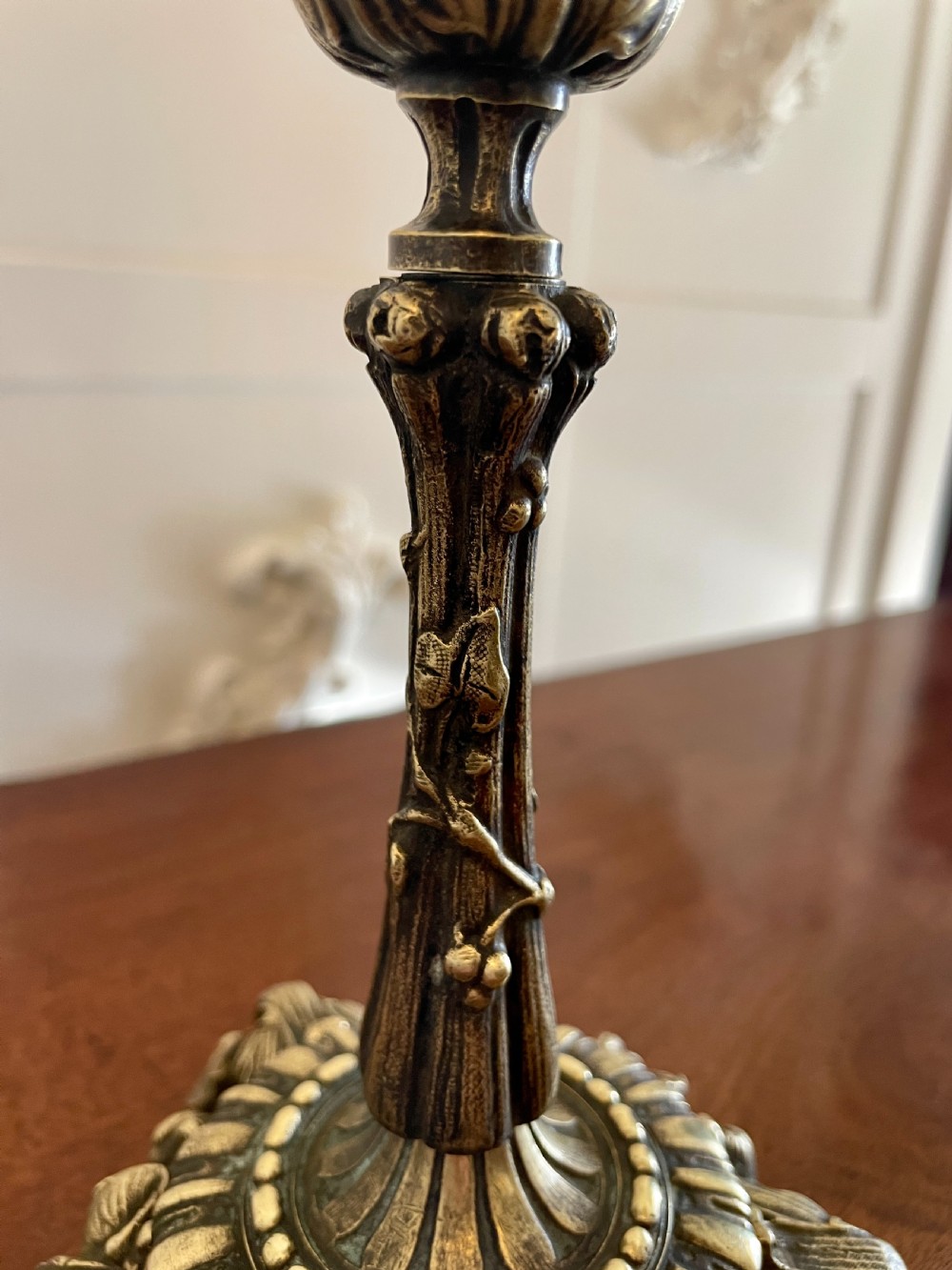 A pair of ornate brass candlesticks featuring intricate foliage carving, fluted stems, and scalloped candle sockets. View VIII