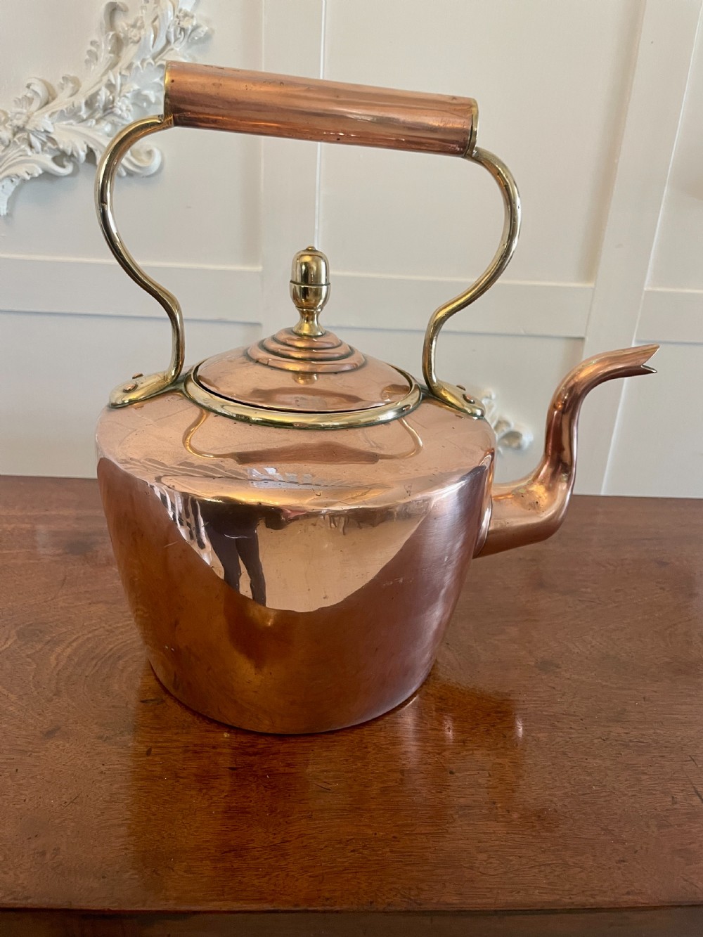 A George III copper tea kettle featuring brass handle mounts, an acorn finial, and a curved spout. View X