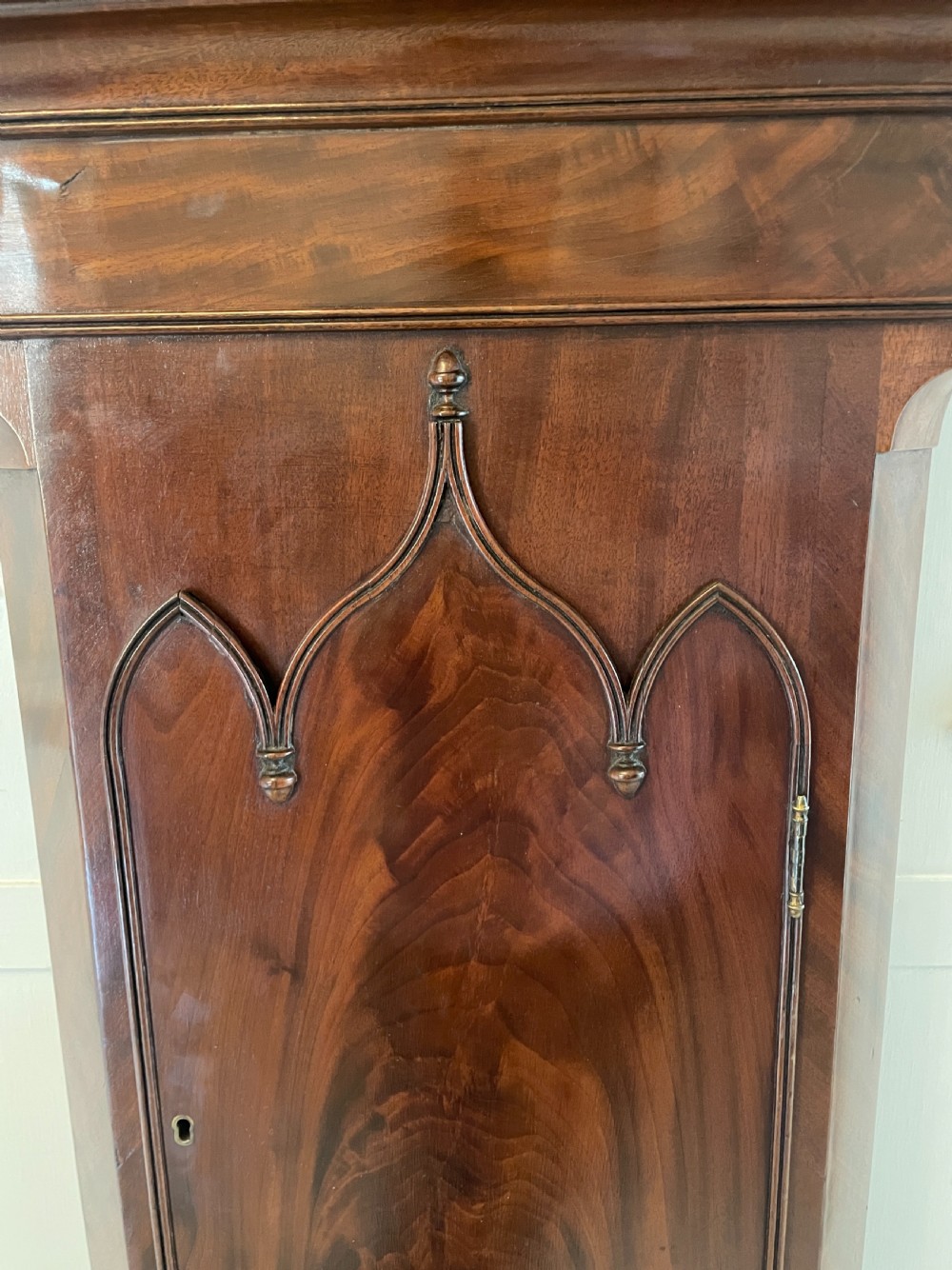 A George III mahogany eight-day longcase clock featuring a swan-neck pediment, turned hood columns, painted dial, and a shaped Gothic trunk door. View VI