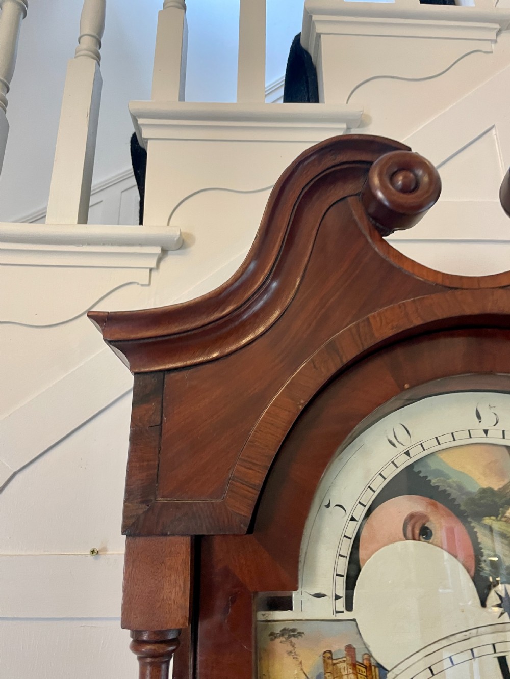 A George III mahogany eight-day longcase clock featuring a swan-neck pediment, turned hood columns, painted dial, and a shaped Gothic trunk door. View XII