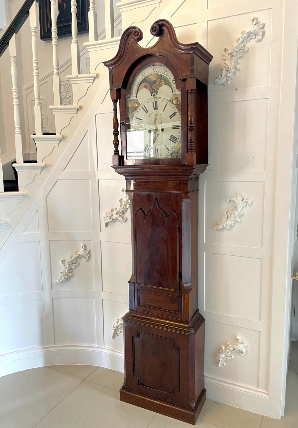 A George III mahogany eight-day longcase clock featuring a swan-neck pediment, turned hood columns, painted dial, and a shaped Gothic trunk door. View XVI